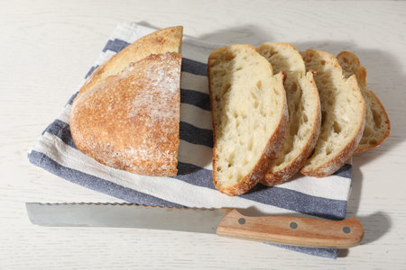 Loaf of fresh bread and knife on white wooden table, above view