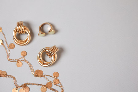 Stylish presentation of gold jewelry on light background, flat lay. Space for text