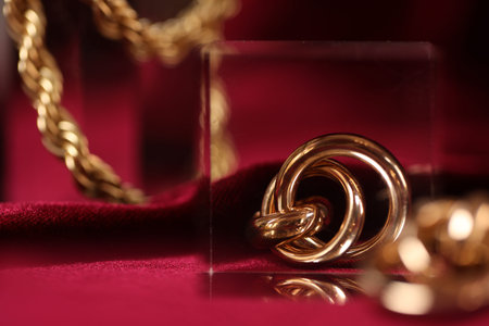 Stylish gold jewelry on red cloth, closeup. Space for text