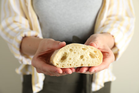Woman holding half of fresh ciabatta on light background, closeup