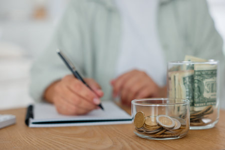 Glass jars with money and woman budgeting at wooden desk, selective focusの写真素材