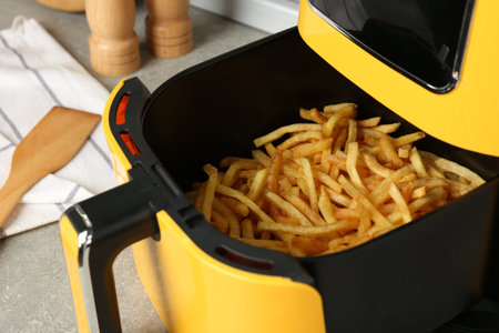 Modern air fryer with cooked French fries on gray background, closeup