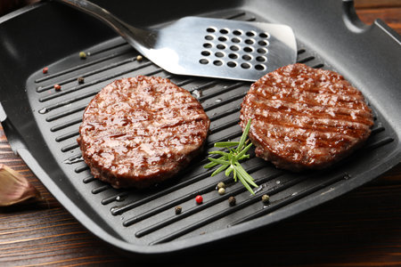 Pan with grilled patties, spices and slotted spatula on wooden table, closeupの写真素材