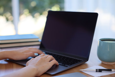 Woman working with laptop at table against blurred background, closeupの写真素材