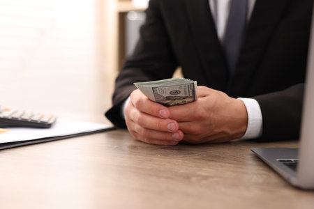 Man counting dollar banknotes at wooden table, closeup
