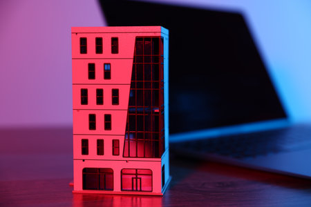 Real estate. Apartment building model and laptop on table in neon lights, closeupの写真素材