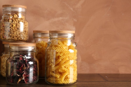Glass jars with different products on wooden table, closeup. Space for textの写真素材