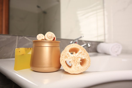 Loofah sponge and cosmetic products on sink in bathroomの写真素材