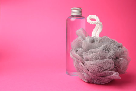 Gray shower puff and bottle of cosmetic product on pink background, space for textの写真素材