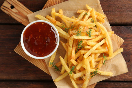 Tasty French fries with sauce on wooden table, top view