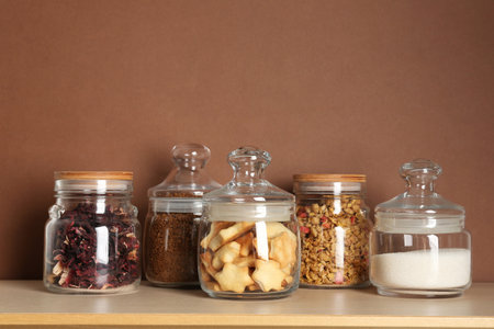 Glass jars with different products on wooden table against brown backgroundの写真素材