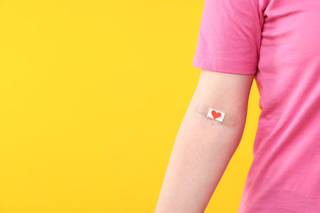 Blood donation. Woman with bandage on arm against yellow background, closeup. Space for textの写真素材