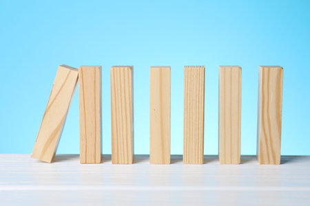 Risk. Wooden blocks falling on white table against light blue background