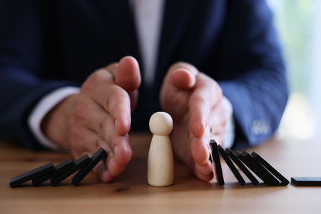 Risk. Man stopping domino effect to protect wooden figure at table, closeupの写真素材