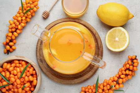 Sea buckthorn tea in teapot, fresh berries, honey and lemon on light gray table, flat layの写真素材