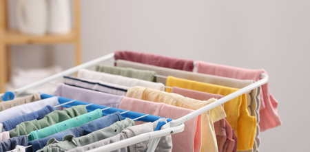 Many clean baby clothes on drying rack indoors, closeup