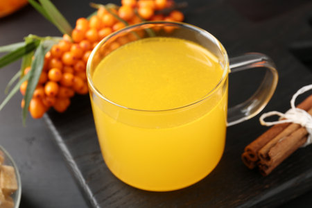 Sea buckthorn tea in glass cup, fresh berries and cinnamon on black table, closeupの写真素材