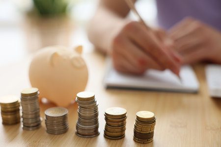 Man working at wooden table indoors, focus on stacks of coinsの写真素材