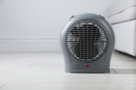 Electric fan heater on light wooden floor indoors, closeup. Space for textの写真素材