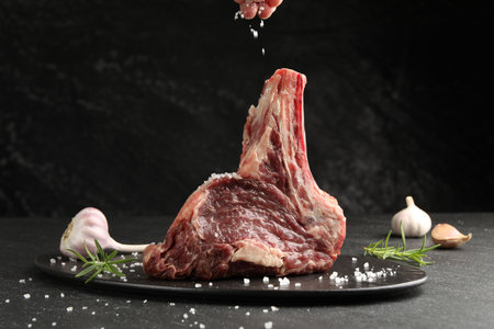 Woman adding spices to raw beef meat at black table, closeupの写真素材