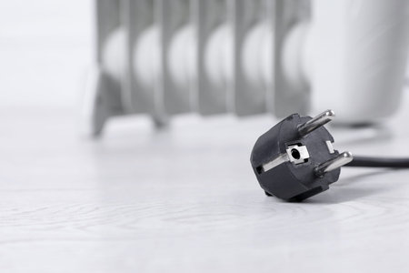 Electric plug of heater on light wooden floor, selective focus. Space for textの写真素材