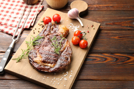 Delicious grilled beef steak with herbs, spices and products on wooden table, closeup. Space for textの写真素材