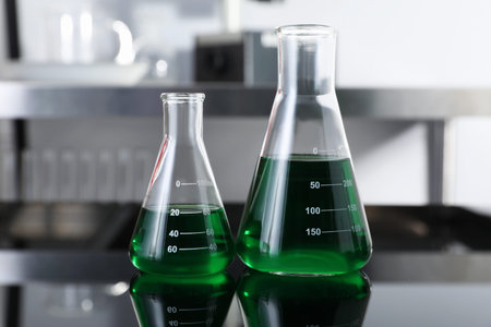 Glass flasks with green liquid on table in laboratory, closeup