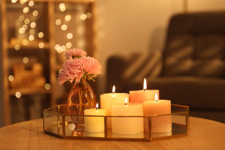 Tray with burning candles and beautiful flowers on wooden table indoors, closeup. Bokeh effect