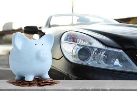 Piggy bank and coins against car outdoors.の写真素材