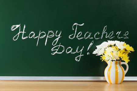 Phrase Happy Teacher's Day written on chalkboard and vase of flowers on wooden tableの写真素材