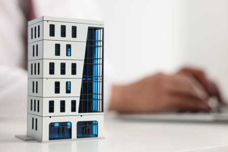 Real estate agent working laptop at white table, focus on apartment building modelの写真素材