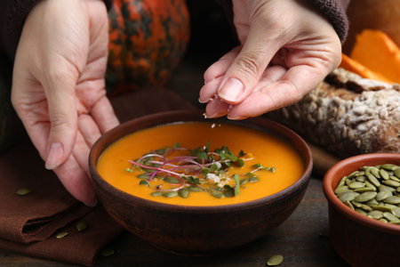 Woman salting delicious pumpkin soup at wooden table, closeupの写真素材