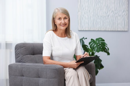 Professional psychotherapist with clipboard in armchair indoorsの写真素材
