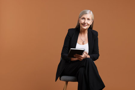 Professional psychotherapist with notebook and pen on chair against brown background, space for textの写真素材