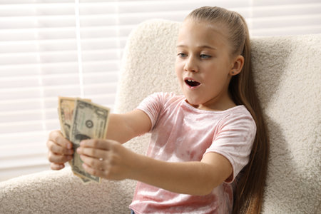 Little girl with pocket money in armchair at homeの写真素材