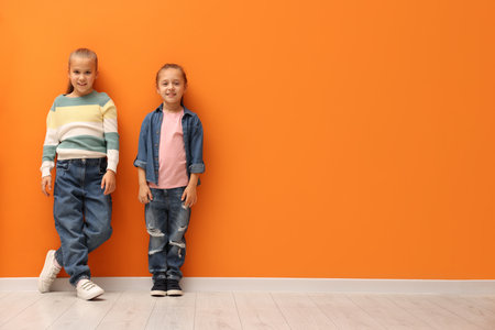 Little girls near orange wall indoors, space for textの写真素材