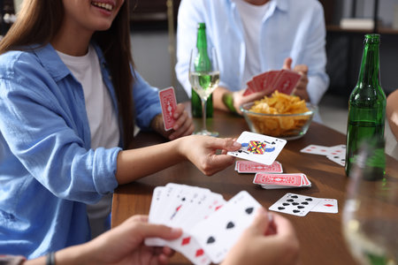 Friends playing cards at wooden table indoors, closeup