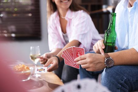 Friends playing cards at table indoors, selective focus