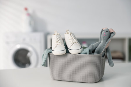 Laundry basket with baby clothes, shoes and toy bunny on white table indoors. Space for textの写真素材