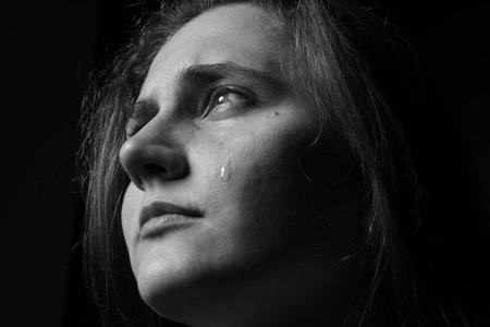 Sad woman crying on dark background, closeup. Black and white effect