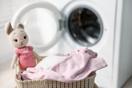 Laundry basket with baby clothes and toy bunny near washing machine, selective focusの写真素材