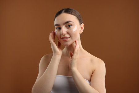 Beautiful woman with cream on her face against brown backgroundの写真素材