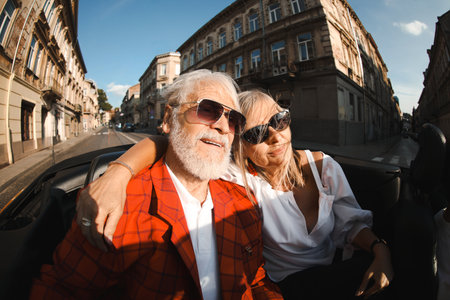 Senior couple enjoying cabriolet ride in city, wide angle lensの写真素材