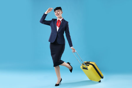 Positive stewardess with suitcase on light blue backgroundの写真素材