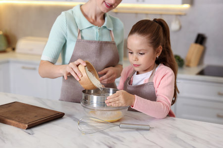 Little helper. Mother and daughter cooking together at white marble table in kitchen