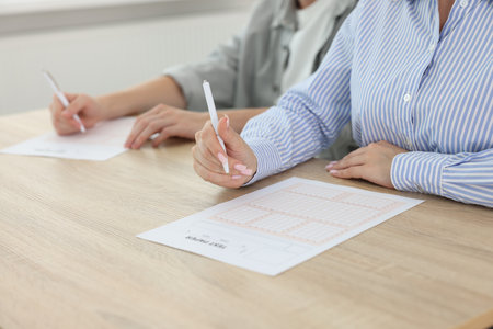 Students filling out answer sheet at wooden table indoors, closeup. Taking examの写真素材