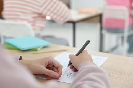 Student filling out answer sheet at wooden table indoors, closeup. Taking examの写真素材