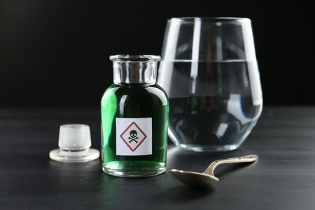 Bottle of poison with warning sign, water and spoon on black wooden table, closeupの写真素材