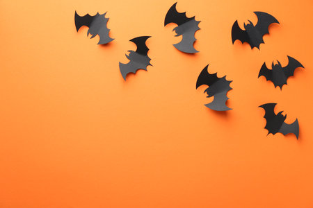 Halloween decor. Black paper bats on orange background, flat lay. Space for textの写真素材