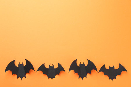 Halloween decor. Black paper bats on orange background, flat lay. Space for textの写真素材